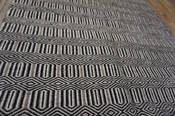 Black and shades of gray geometric rug featuring repeating oblong and diamond shapes on wood flooring.