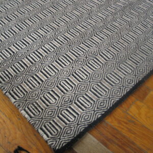 Black, gray, and cream geometric rug with repeating hexagon and diamond shapes on wood flooring.