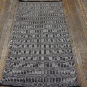 Flat-woven black and white geometric runner rug on rustic wood plank flooring.