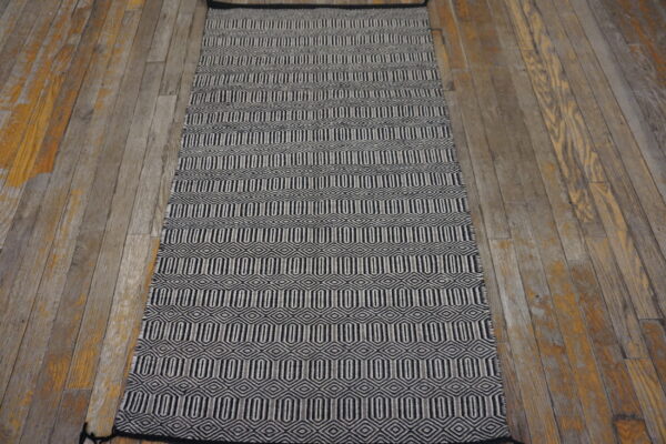 Flat-woven black and white geometric runner rug on rustic wood plank flooring.