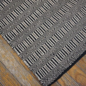 Geometric rug in alternating black and gray stripes forming hexagonal shapes on rustic wood floorboards.