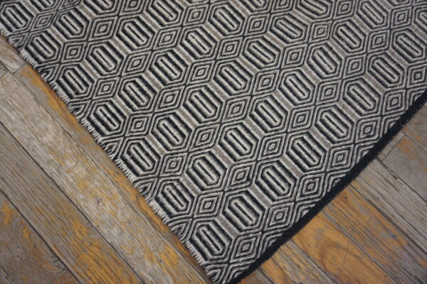 Geometric rug in alternating black and gray stripes forming hexagonal shapes on rustic wood floorboards.