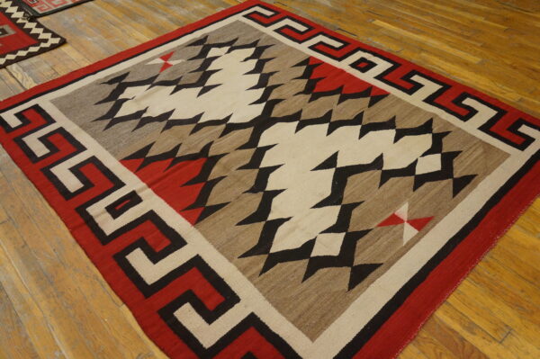 Red, black, tan, and cream flat-woven rug with a zigzag design and geometric border on wood.