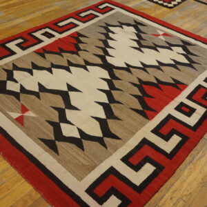 Red, black, beige, and brown geometric flatweave rug with a meander border on light wood flooring.