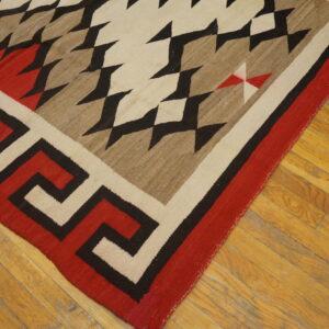 Red, black, cream, and brown flatwoven rug with geometric and key patterns on a wood plank floor.