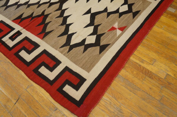Red, black, cream, and brown flatwoven rug with geometric and key patterns on a wood plank floor.