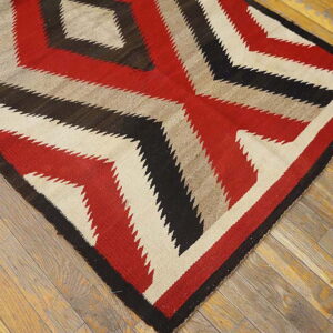 Red, black, and beige flatweave rug with a serrated geometric design on weathered wood.