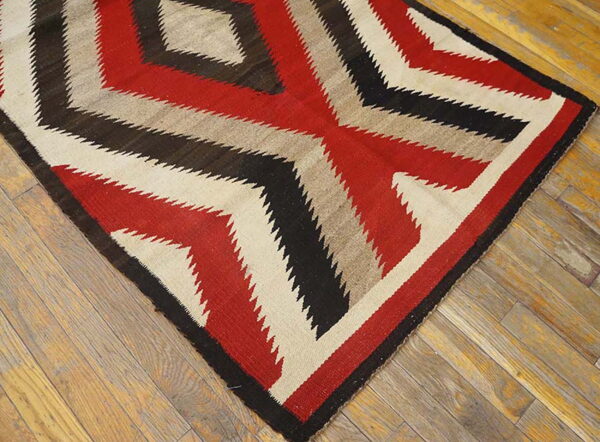 Red, black, and beige flatweave rug with a serrated geometric design on weathered wood.