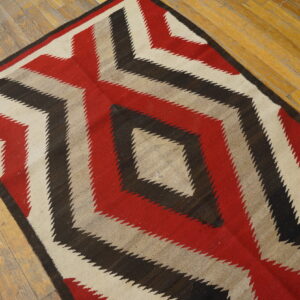 Geometric rug in red, black, cream, and tan with stepped diamond pattern on distressed wooden planks.