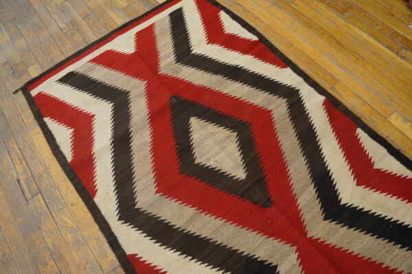 Geometric rug in red, black, cream, and tan with stepped diamond pattern on distressed wooden planks.