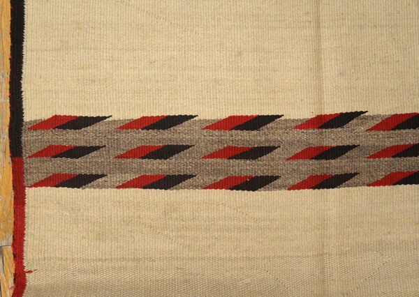 Flatweave rug features a tan field and a central band of red and black geometric designs.