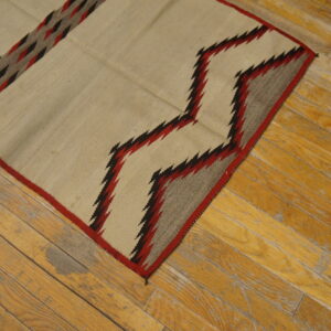 Cream flatweave rug featuring red, black, and gray zigzag patterns on distressed wood flooring.