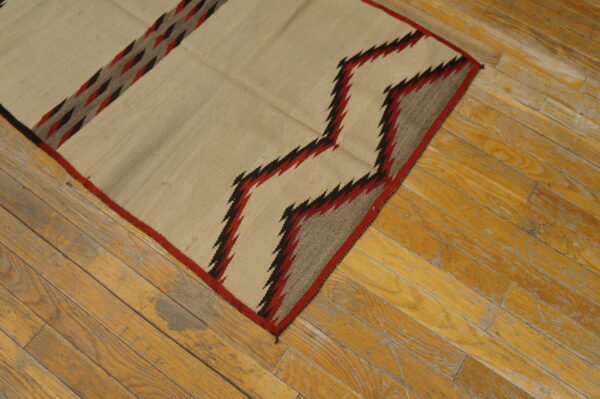 Cream flatweave rug featuring red, black, and gray zigzag patterns on distressed wood flooring.
