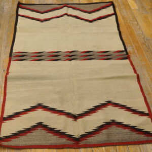 Flatwoven cream rug with red, black, and gray geometric zigzag patterns rests on wood plank flooring.