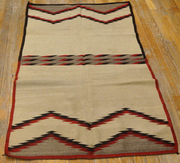 Flatwoven cream rug with red, black, and gray geometric zigzag patterns rests on wood plank flooring.