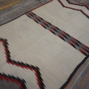 Flatwoven cream rug with black, red, and gray geometric zigzags and diamonds on rustic wood planks.