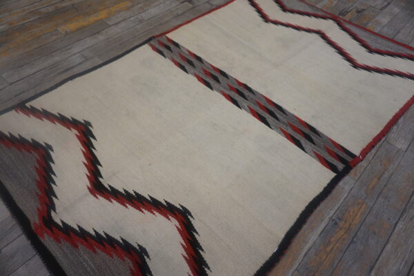 Flatwoven cream rug with black, red, and gray geometric zigzags and diamonds on rustic wood planks.