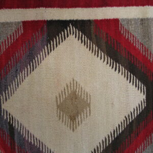 A flatwoven rug with a large central beige diamond, framed by serrated geometric shapes in red, gray, and dark brown.