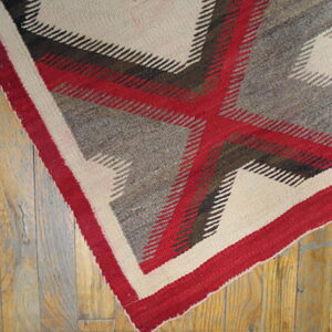 Red, grey, and cream geometric flat-weave rug featuring a large cross pattern on distressed wood flooring.