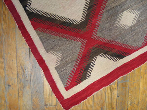Red, grey, and cream geometric flat-weave rug featuring a large cross pattern on distressed wood flooring.