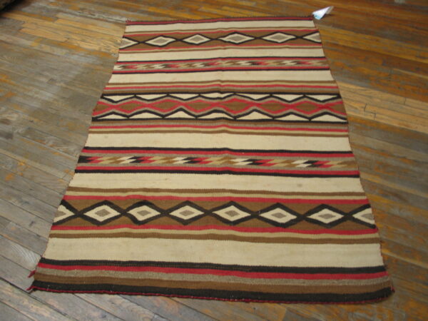 Cream, brown, red, and black geometric rug featuring stripes and diamonds rests on distressed wood flooring.