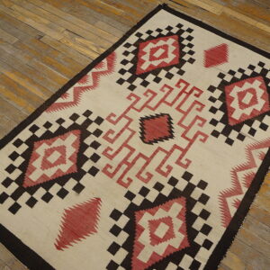 Cream flatweave rug featuring sharp red and dark brown diamond and stepped geometric patterns on wood planks.