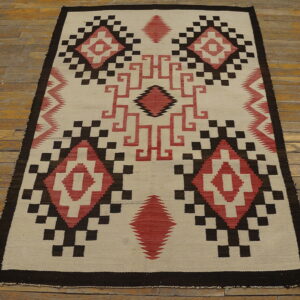 Geometric flatweave rug in cream, dark brown, and red diamonds rests on rustic wood planks.