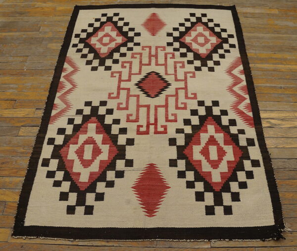 Geometric flatweave rug in cream, dark brown, and red diamonds rests on rustic wood planks.