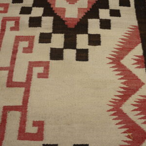 Flatweave rug featuring geometric stepped and meander patterns in cream, red, and dark brown on wood flooring.