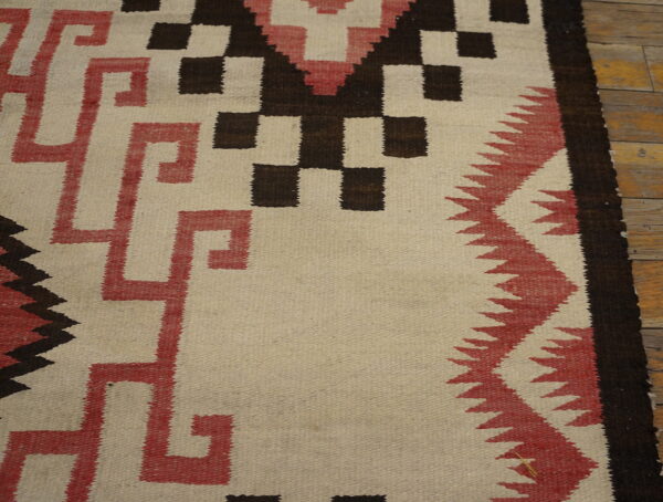 Flatweave rug featuring geometric stepped and meander patterns in cream, red, and dark brown on wood flooring.
