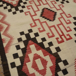 Cream flatweave rug featuring sharp red and dark brown geometric patterns on wood floors.