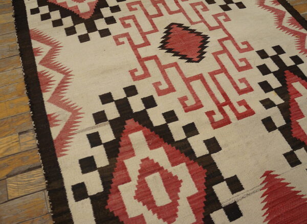 Cream flatweave rug featuring sharp red and dark brown geometric patterns on wood floors.