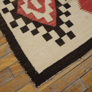 Tight-woven rug featuring geometric patterns in cream, dark brown, and red on aged wooden floorboards.