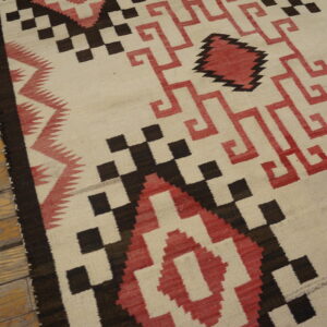 Cream flatweave rug featuring stepped geometric designs in dark brown and terracotta red on wood floor.