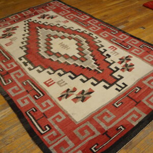 Red, cream, and gray geometric rug with a stepped central medallion on distressed wood floors.