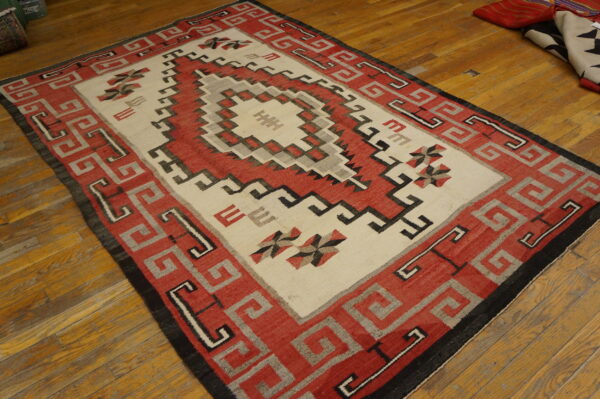 Red, cream, and gray geometric rug with a stepped central medallion on distressed wood floors.