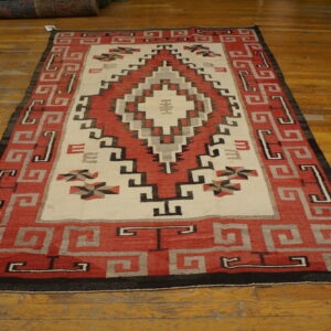 Geometric red, cream, gray, and black flat-weave rug displayed on distressed hardwood flooring.