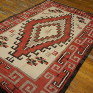Red, cream, black, and gray geometric flat-weave rug with a stepped medallion on wood flooring.