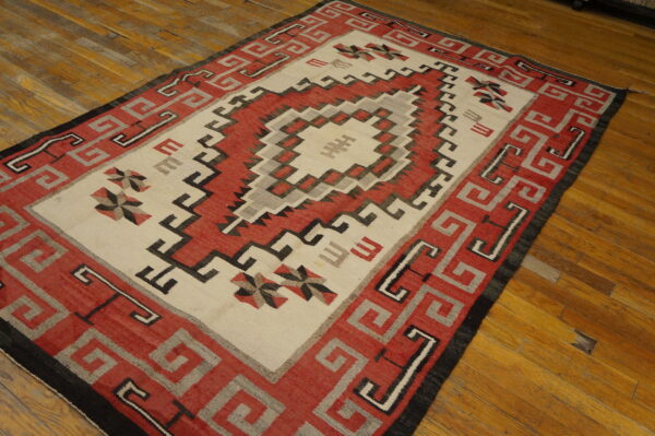 Red, cream, black, and gray geometric flat-weave rug with a stepped medallion on wood flooring.