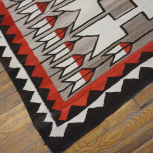 Flatwoven rug featuring red, black, white, and gray geometric patterns rests on distressed hardwood flooring.