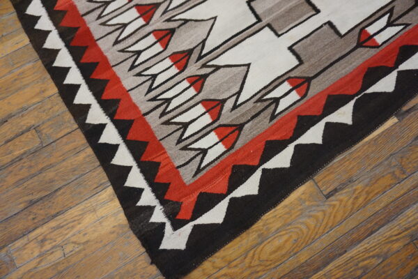 Flatwoven rug featuring red, black, white, and gray geometric patterns rests on distressed hardwood flooring.
