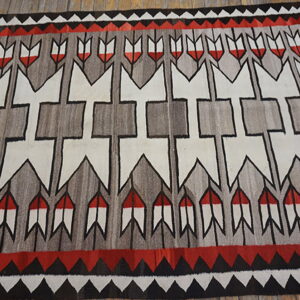 Red, gray, black, and white geometric rug with arrows and borders on wood flooring.