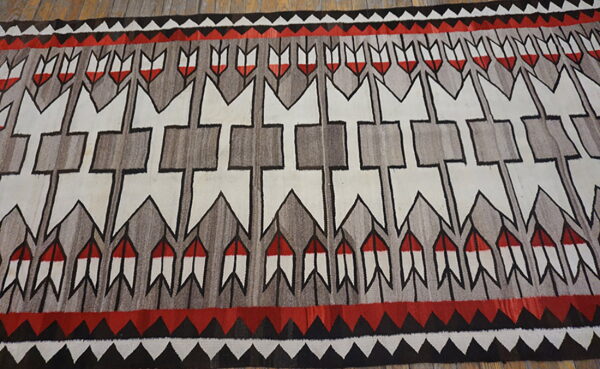 Red, gray, black, and white geometric rug with arrows and borders on wood flooring.