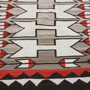 Low-pile geometric rug in white, gray, red, and black with central repeating hourglass patterns.