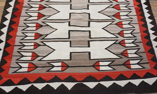 Low-pile geometric rug in white, gray, red, and black with central repeating hourglass patterns.