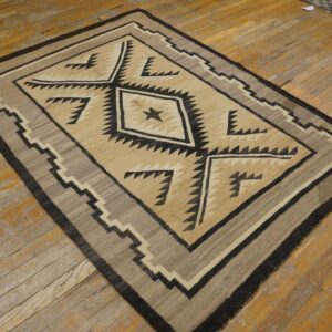 Beige and black geometric rug with serrated borders rests on worn, light brown wood planks.