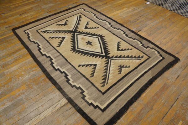 Beige and black geometric rug with serrated borders rests on worn, light brown wood planks.