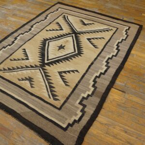Geometric flatweave rug in tan, black, and gray with central diamond patterns rests on distressed wood flooring.