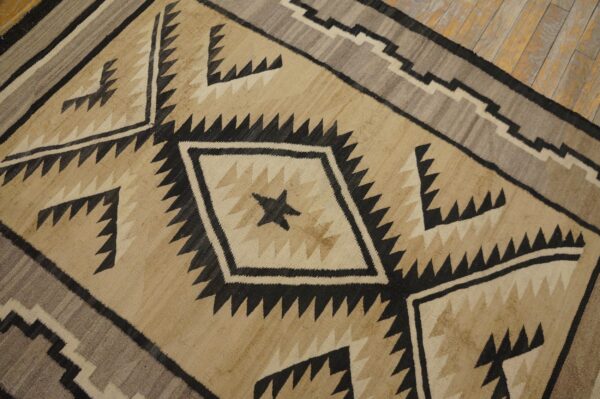 Geometric rug in tan, cream, gray, and black with serrated diamonds on worn wooden floorboards.