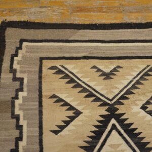 Tan, gray, and black geometric flatweave rug detail on a distressed yellow wood floor.